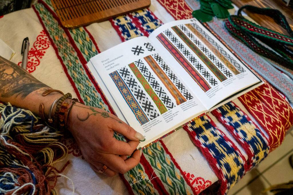 Na stole na którym leżą słowiańskie krajki leży otwarta książka ze wzorami do ich tkania.
