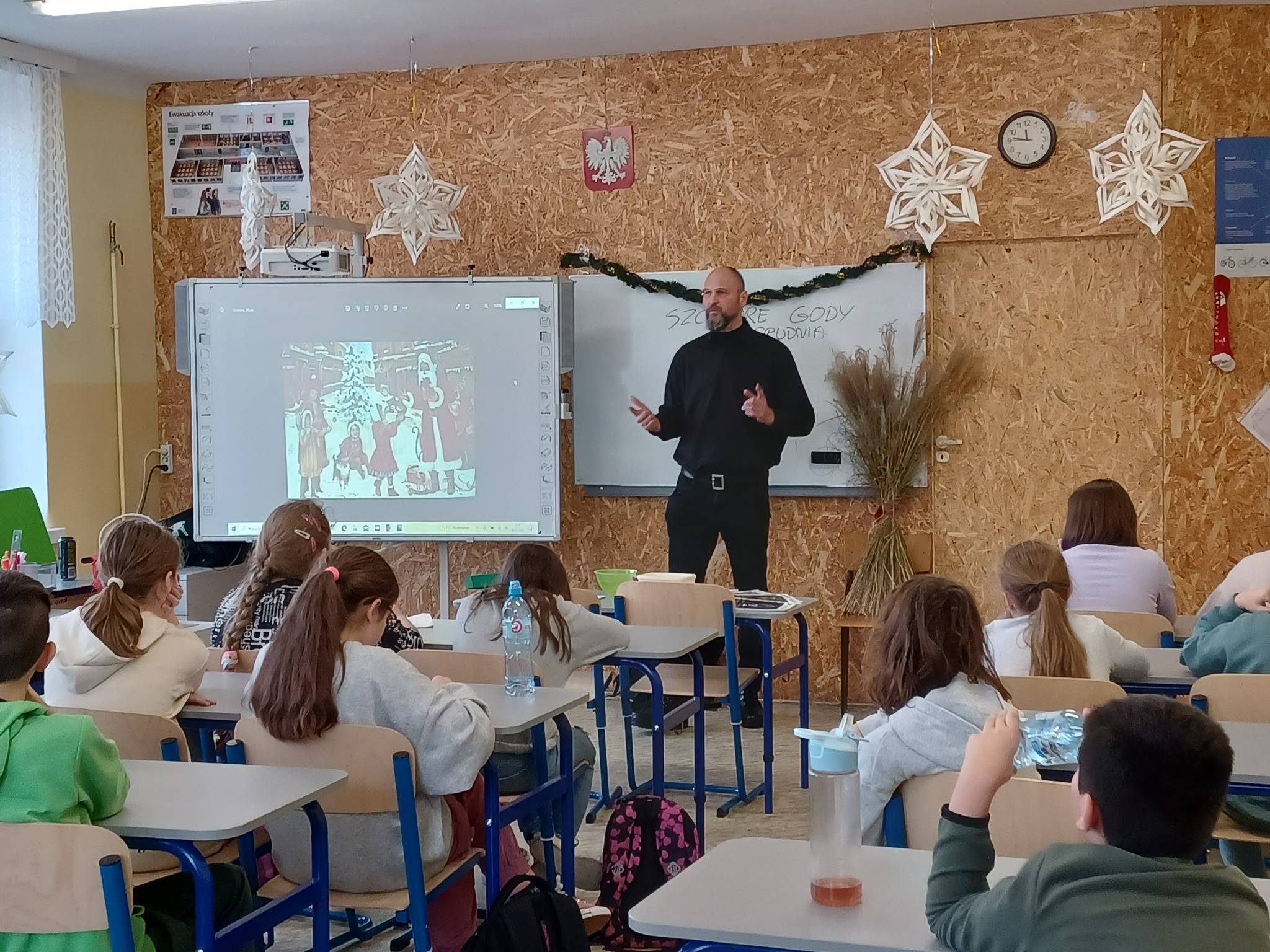 Fundacja Rodzima Ziemia. Wykład prowadzony przez Marcina Sadowskiego dla dzieci w szkole podstawowej na temat tradycji ludowych i słowiańskich korzeni. Na tablicy jest napisany temat wykładu "Szczodre Gody".