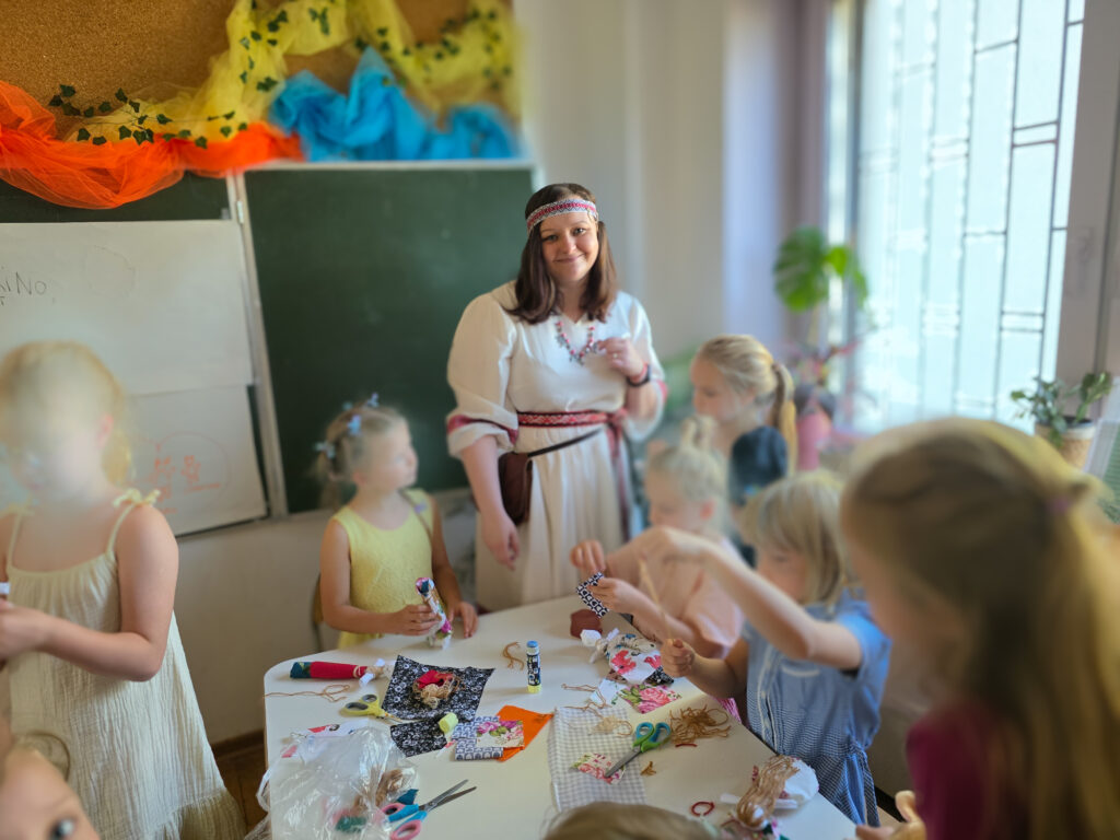 Marlena Jurczak w szkolnej sali ubrana w słowiańską suknię, prowadząca warsztaty w szkole podstawowej z tworzenia motanek 
